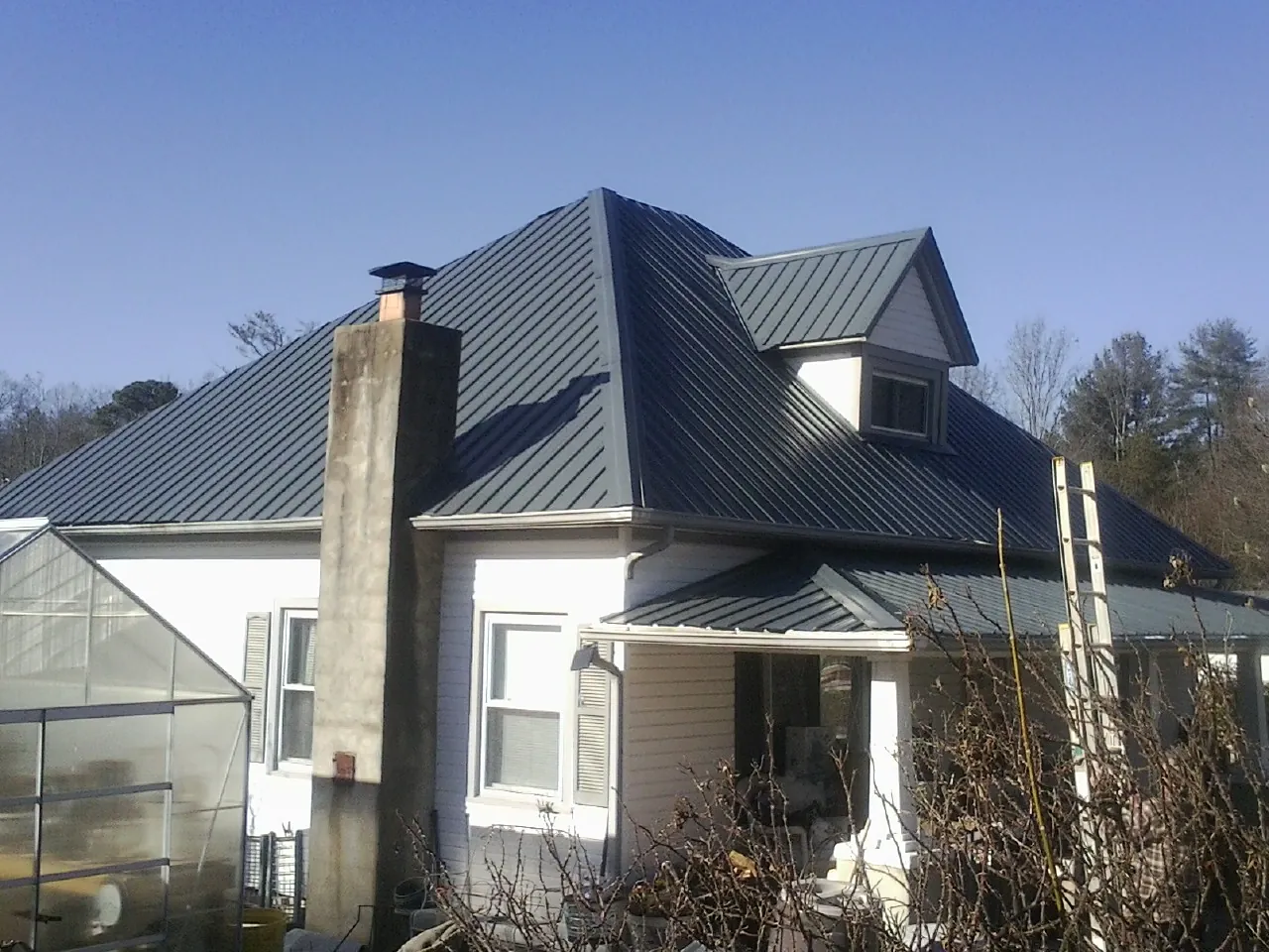 Dark blue standing seam metal roof on a white farmhouse with dormer — Slate & Tile Roof Repair by Roofing Brothers in Lonsdale