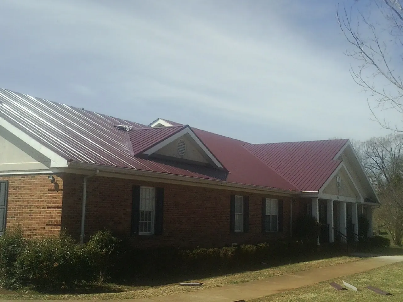 Red metal roof with gabled entries on a long brick building, from a Hail Damage Roof Repair job in Lonsdale