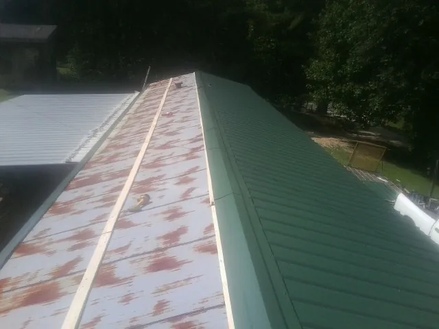 Old rusted panels beside newly installed green metal roofing — Wind Damage Roof Repair by Roofing Brothers in Lonsdale