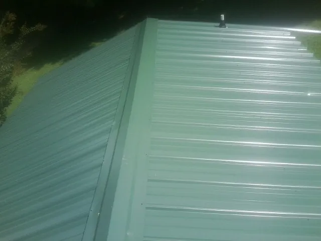 New green metal panels meeting at the ridge of a roof — Flat Roof Repair work by our crew in Lonsdale