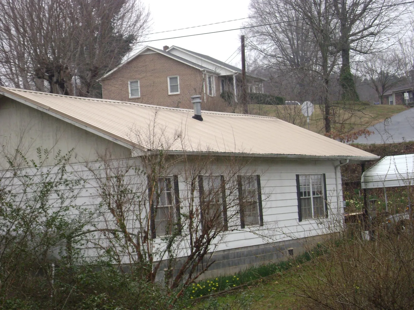Tan metal roof on a white sided house set into a hillside — Commercial Roofing by Roofing Brothers in Lonsdale