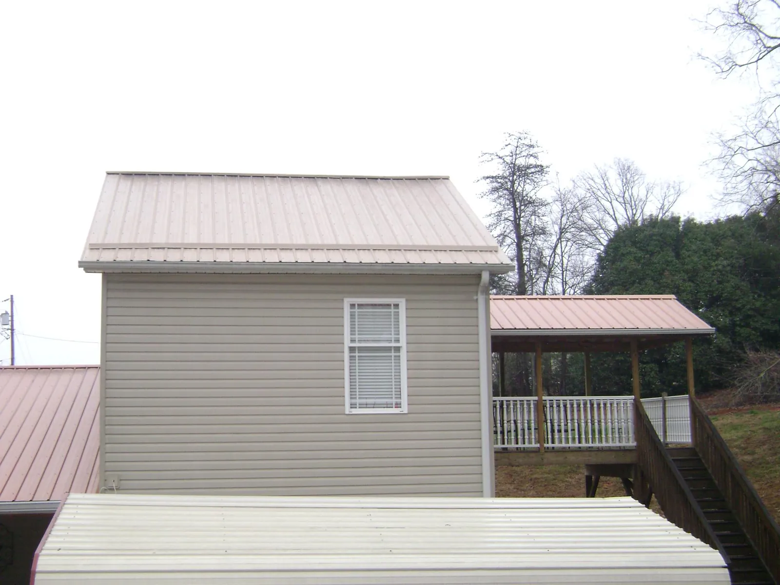 Tan metal roofs on a two story addition and attached porch, from a Roof Replacement job in Lonsdale